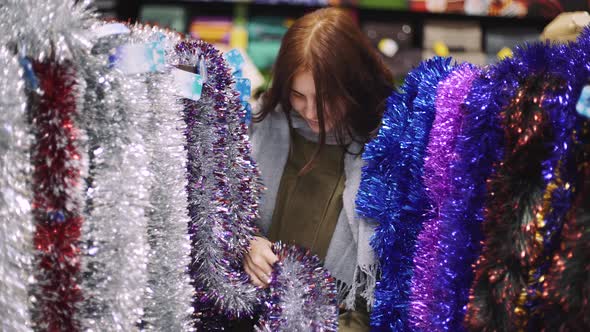 A Young Beautiful Woman Walks Around the Store and Selects Christmas Decorations and Decorations to alt