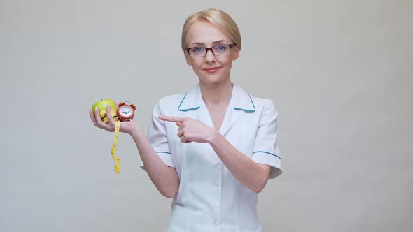 Nutritionist Doctor Healthy Lifestyle Concept - Holding Green Apple, Alarm Clock and Measuring Tape alt