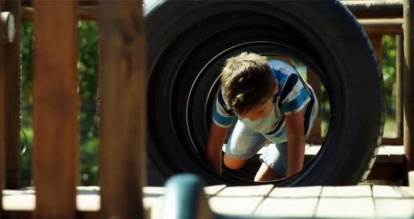 Schoolboy crawling through tyres in playground alt