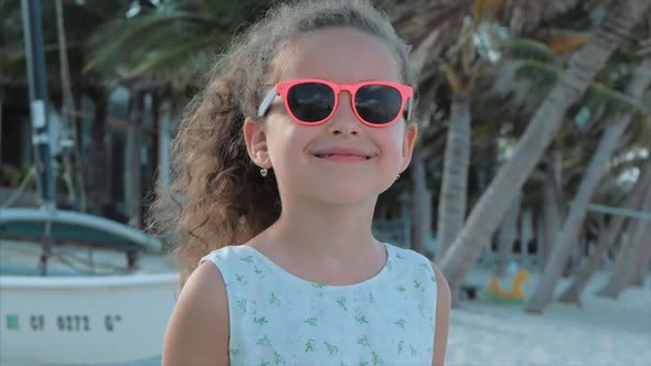 Close-up Portrait of a Beautiful Little Girl in Pink Glasses, Cute Smiling, Looking at the Camera alt