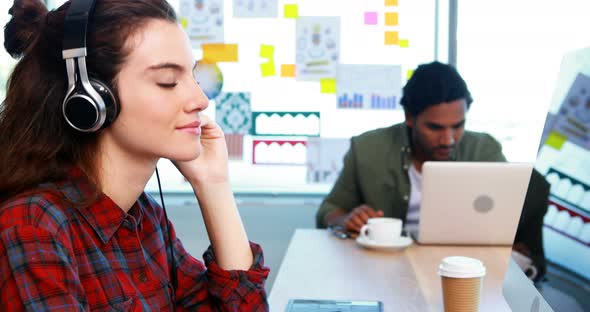 Female graphic designer working while listening music at desk alt