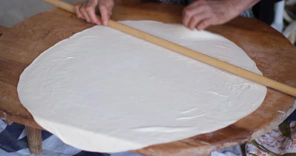 Female Hands Of Baker Rolls Dough In Flour On Wooden Board On Table With A Rolling Pin