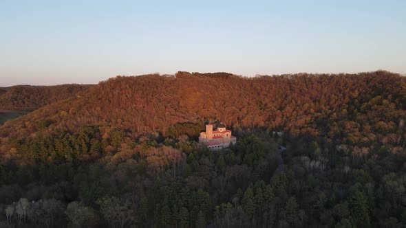 Panoramic view of church nestled into pocket in forest on mountain at sunset.