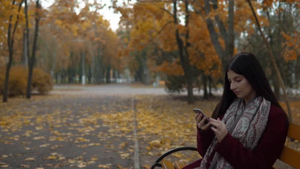 Woman on Bench in Park Using Smartphone