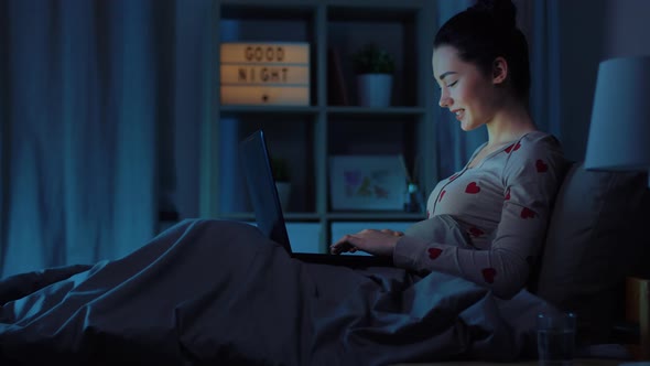 Teenage Girl with Laptop in Bed at Home at Night