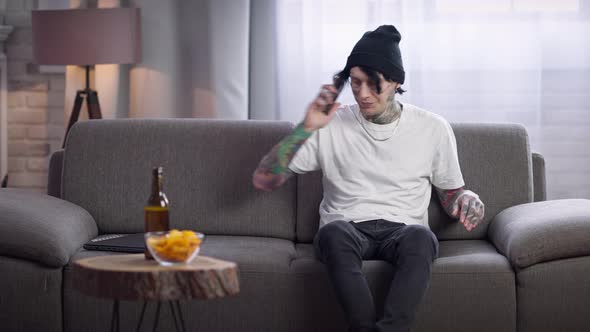 Portrait of Stressed Young Tattooed Man Talking on Phone Hanging Up Holding Head in Hands alt