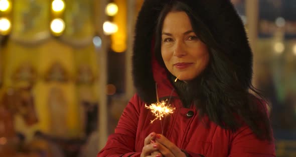 Portrait of Positive Caucasian Woman in Red Coat Holding Sparklers and Smiling. Happy Adult Lady alt