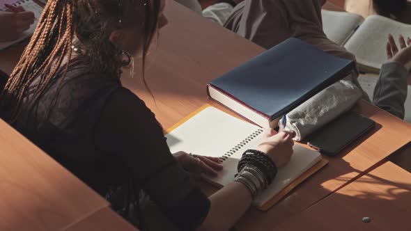 Female Student with Dreadlocks Taking Notes in Copybook alt