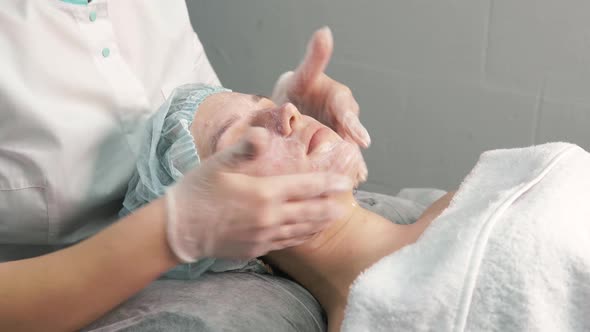 The Cosmetologist Distributes a White Moisturizing Nourishing Cream on the Face