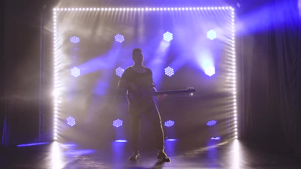 Silhouette of a Young Guy Playing on the Electric Guitar on Stage in a Dark Studio with Smoke and alt