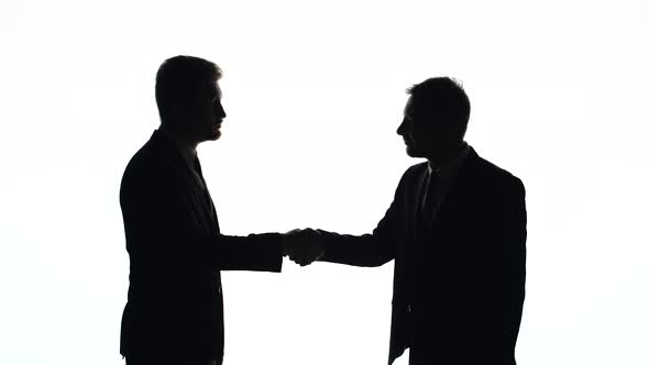 Silhouettes of Men in Business Suits Shake Hands on a White Background in Studio alt