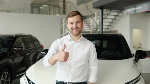 Portrait of a Young Man Near a New Electric Car in a Car Dealership alt