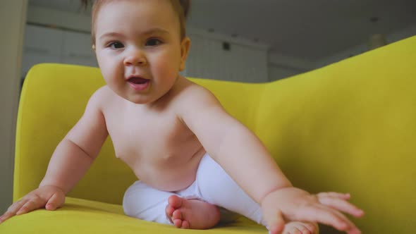 the Portrait of the Baby Girl Playing on the Yellow Sofa at Home in the Living Room alt