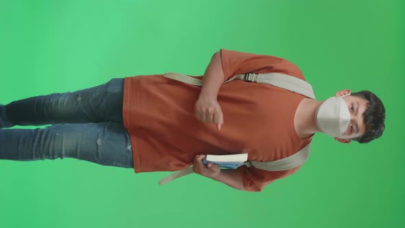 Asian Boy Student Wearing A Mask, Holding A Book And Running To School On Green Screen alt