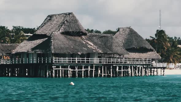 African Restaurant with Thatched Roof on Wooden Poles Above the Ocean alt