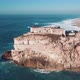 Aerial view of Nazare seascape, old Fortress and lighthouse on cliff; blue stormy water of Atlantic - VideoHive Item for Sale