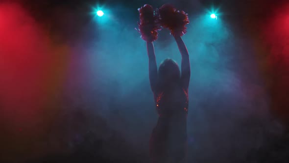 Silhouette of Cheerleader Dancing with Pompoms Against Background of Smoke and Bright Blue and Red alt