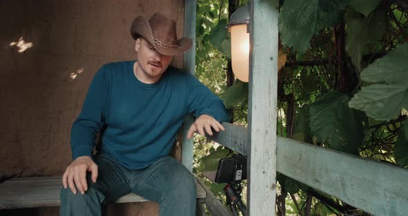 Cowboy Man Communicates Online Using His Phone While Sitting on Porch