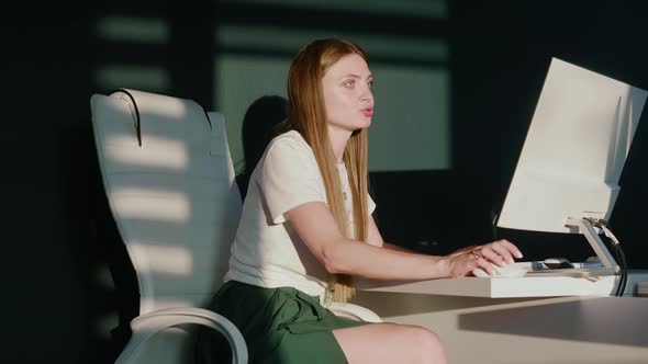 Caucasian Woman Works in an Office at Computer in the Rays of the Setting Sun