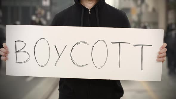 Unknown Rioter Holds a Placard with BOYCOTT Text alt