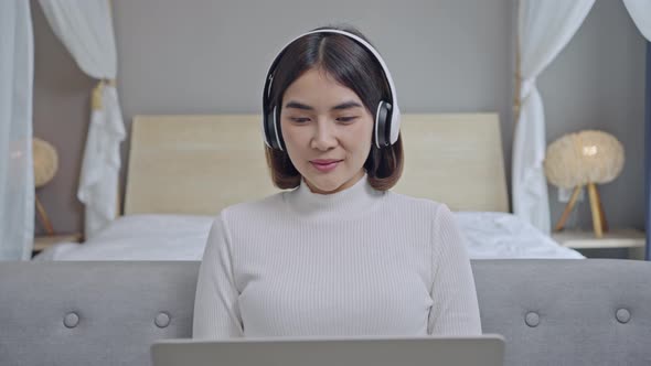 Happy young woman wear wireless headphones make video call online at laptop screen sit on sofa. alt