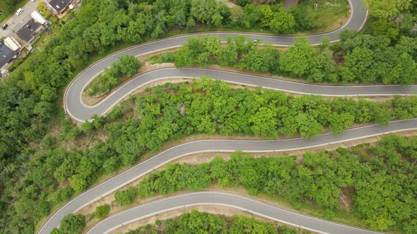 Cars driving up a long curvy switchback road in west Germany. Ascending high angle drone footage alt