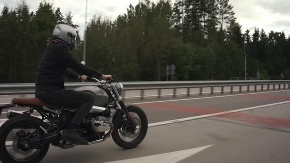 Man Riding Scrambler Motorbike on the Highway Through the Autumn Forest alt