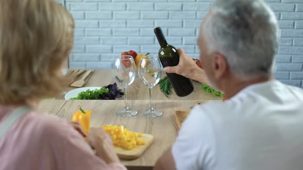 Romantic Man Pouring Red Wine in Glasses, Happy Couple Cooking Together at Home alt