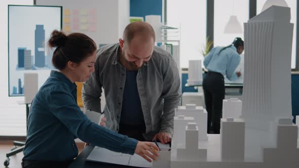 Team of Coworkers Analyzing Building Model and Blueprints Plan on Table to Design Construction alt