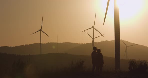 Two Young Men Standing Near the Wind Turbines Pointing Their Hand Forward, Silhouette Shooting alt