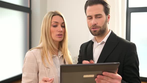 Beautiful Woman and Serious Man with a Digital Tablet in Hands is Standing at the Office