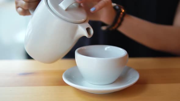 Close Up View of Female Hands Pouring Hot Tea From the Teapot in the White Porcelain Cup on the alt