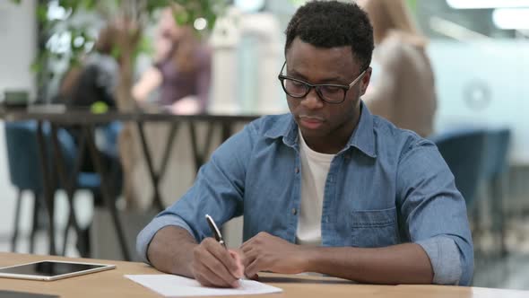 Hardworking Young African Man Writing on Paper in Modern Office alt