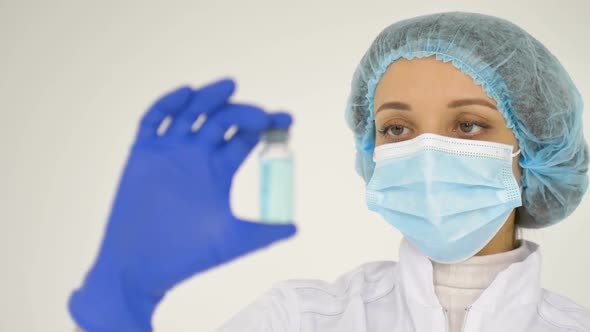 A Female Doctor in a Face Mask and in Medical Blue Gloves Shows a Ampoule with Coronavirus Vaccine alt