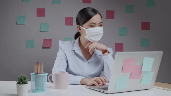 Asian woman wearing protective face mask working on a laptop