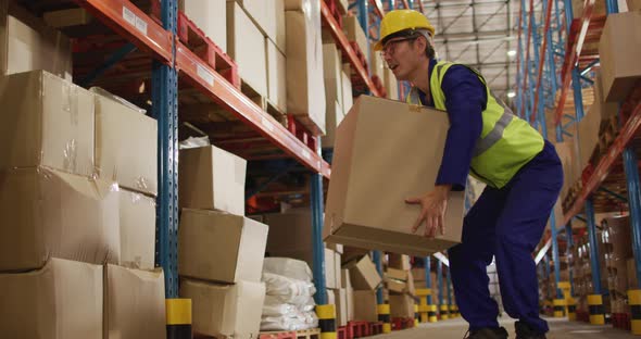 Asian male worker wearing safety suit with helmet and carrying boxes in warehouse alt