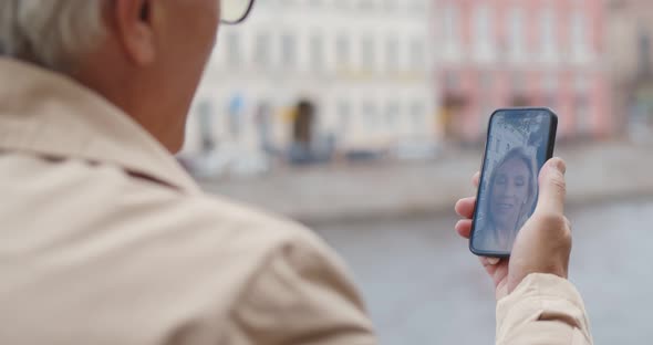 View Over Shoulder of Happy Senior Man Having Video Call on Smartphone in City alt