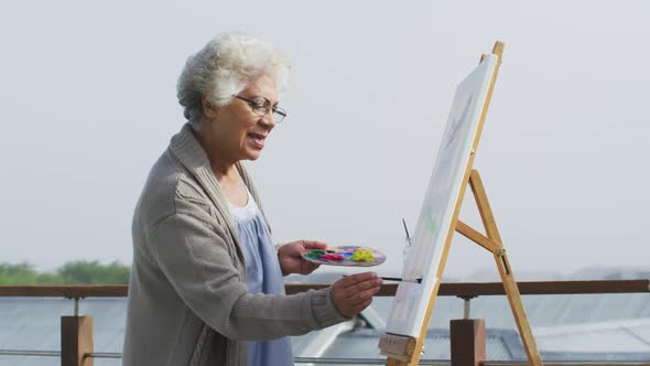 African american senior woman painting on canvas in the balcony at home alt
