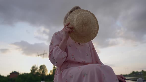 Positive Confident Caucasian Trans Woman in Pink Dress Hiding with Straw Hat Opening Smiling Face alt