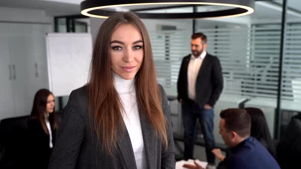 Businesswoman Standing in a Modern Office Building with Colleagues in the Background