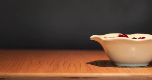 Hand Serving A Fruit Cereal Bowl On Wooden Table With Black Background - Closeup Shot alt
