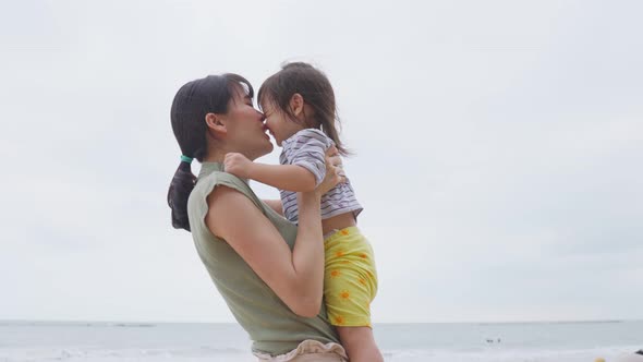 Asian family on vacation. Beautiful mother giving warm hugs little baby girl and rise kid into air. alt