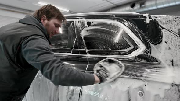 A Man Making Manual Car Wash on a Black Car with Special Cleaning Glove alt