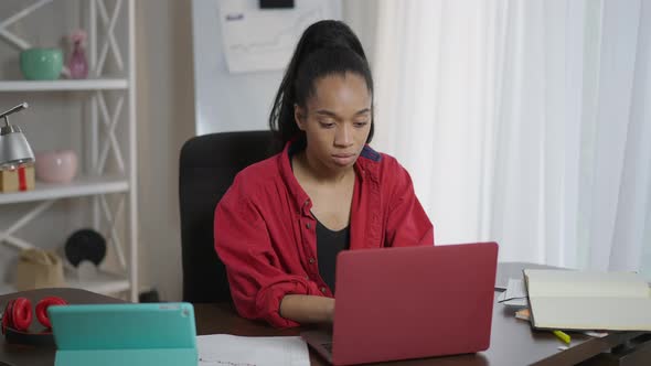 Concentrated Young African American Woman Surfing Internet on Laptop Sitting at Table alt