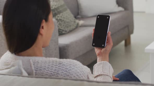 Back view of asian woman sitting on sofa, resting with smartphone with copy space at home alt