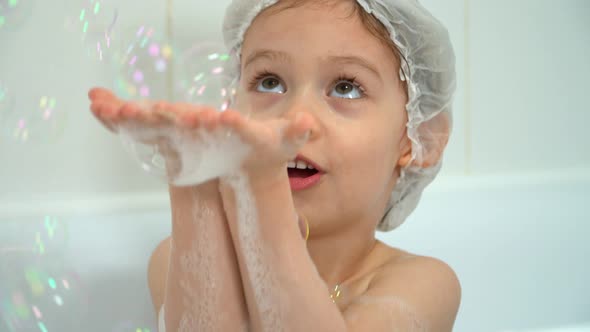 Little Girl Bathes and Plays with Soap Bubbles in Bath