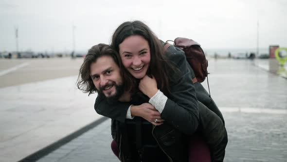 Happy Handsome Man Holding Joyful Girlfriend on His Back alt