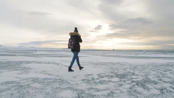 Young Beautiful Woman Traveler with Camera Walking on Snow Desert in Iceland alt