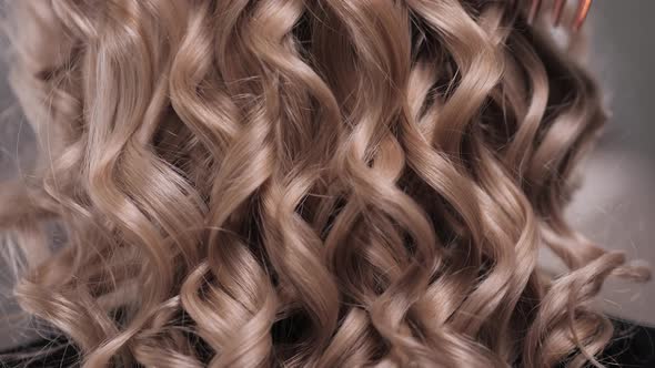 Closeup of a Woman's Hand Combing Her Curled Blonde Hair with a Red Comb alt