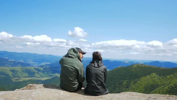 Young Attractive Woman Traveler and Young Attractive Guy Sit on the Top of the Mountain and Look